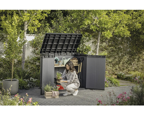 Tuinscene met open gereedschapskast waarin een vrouw tuingereedschap opbergt.