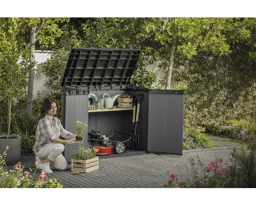 Een vrouw plant bloemen voor een open tuinkast met tuingereedschap