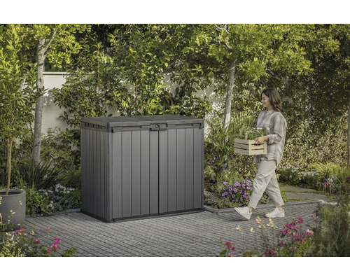 Kunststof tuinkast in de tuin met vrouw die een mand met planten draagt