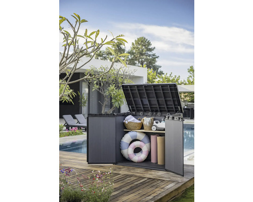 Geopende kunststof tuinkast op een houten terras, gevuld met tuinaccessoires
