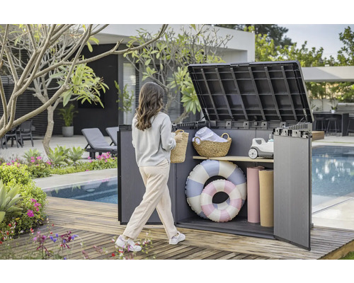Tuinscene met een vrouw die naar een open opbergbox op een houten terras bij het zwembad loopt
