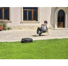 Een robotmaaier maait het gazon terwijl iemand in de tuin zit.