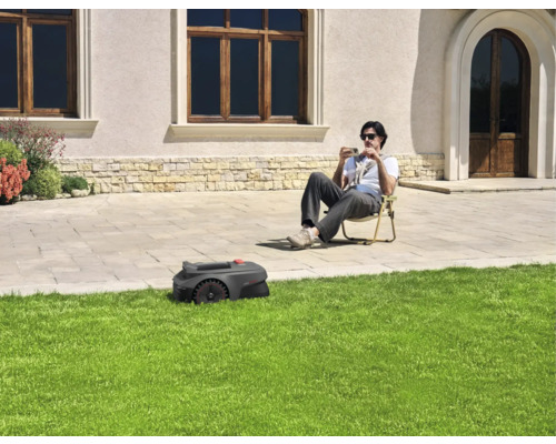 Een robotmaaier maait het gazon terwijl iemand in de tuin zit.