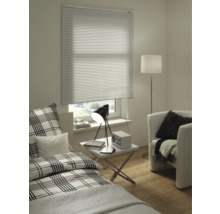 Woonkamer met bed, fauteuil, staande lamp, tafel en raam met jaloezie