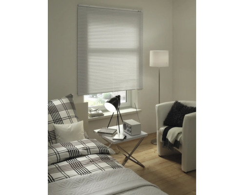 Woonkamer met bed, fauteuil, staande lamp, tafel en raam met jaloezie