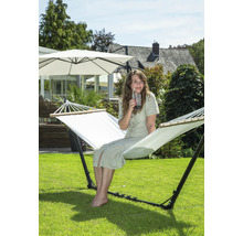 Vrouw zit in een vrijstaande hangmat in de tuin en drinkt een drankje.