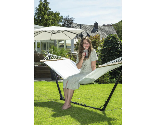 Vrouw zit in een vrijstaande hangmat in de tuin en drinkt een drankje.