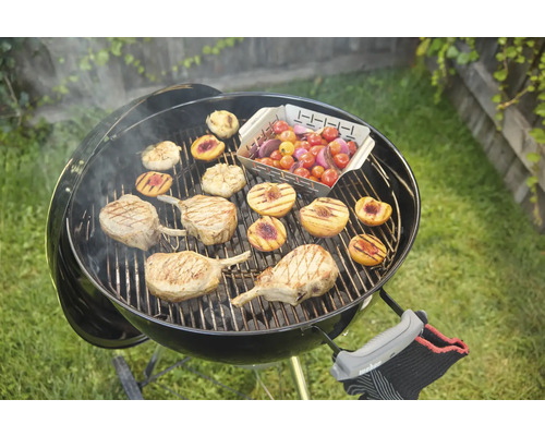 Bolvormige barbecue met gegrild voedsel zoals vlees, perziken en tomaten op het rooster