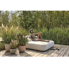 Man ontspant met koptelefoon op een loungesofa in de tuin, omringd door plantenbakken met siergrassen.