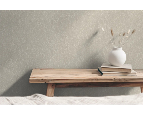 Close-up van een gestructureerd behang in een interieur met een houten bank, boeken en een bloemenvaas als decoratie.