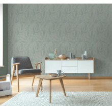 Woonkamer met behang met bladmotief, fauteuil, dressoir en tafel op vloerkleed