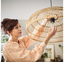 Vrouw vervangt een gloeilamp in een hanglamp van rotan