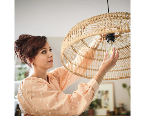 Vrouw vervangt een gloeilamp in een hanglamp van rotan