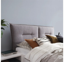 Grijs stoffen hoofdeinde met knopen boven een bed met kussens en dekbed