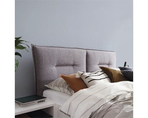 Grijs stoffen hoofdeinde met knopen boven een bed met kussens en dekbed