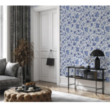 Woonkamer met bloemetjesbehang, bank, kruk en decoraties voor een gezellige sfeer