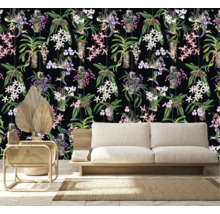 Kamerweergave met een behang met orchideeën en kolibriemotief achter een bank, een fauteuil en een gedroogde palm.