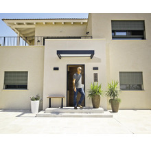 Modern huis met lichte gevels, grijze rolluiken, een zwarte deurluifel boven de voordeur en grote plantenbakken bij de entree.