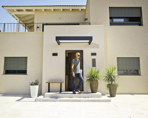 Modern huis met lichte gevels, grijze rolluiken, een zwarte deurluifel boven de voordeur en grote plantenbakken bij de entree.