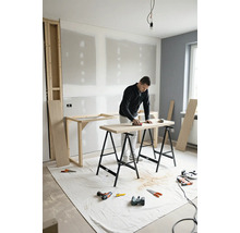 Man schuurt houten plaat op twee schragen in een ruimte