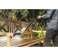 Iemand reinigt een houten bank met een hogedrukreiniger in de tuin.