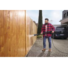 Een man reinigt een houten schutting met een hogedrukreiniger.