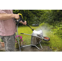 Een man reinigt een kruiwagen met een hogedrukreiniger in de tuin.