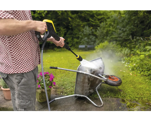 Een man reinigt een kruiwagen met een hogedrukreiniger in de tuin.