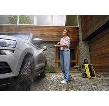 Vrouw reinigt een auto met een hogedrukreiniger van Kärcher voor een huis.