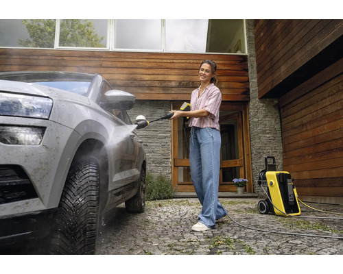Vrouw reinigt een auto met een hogedrukreiniger van Kärcher voor een huis.