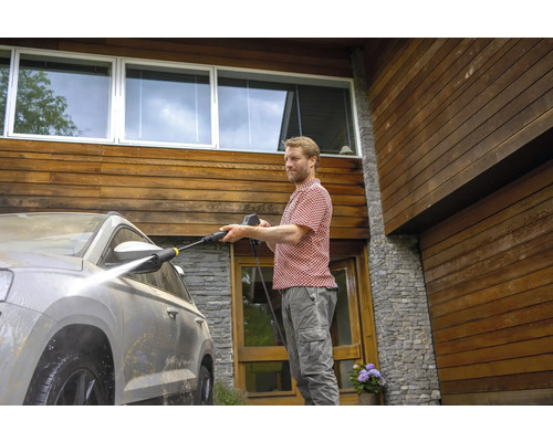 Man reinigt een auto met een hogedrukreiniger voor een huis met een houten gevel