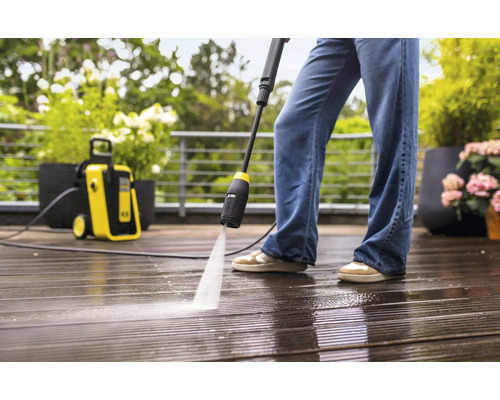 Hogedrukreiniger in gebruik op een houten terras met plantenbakken.