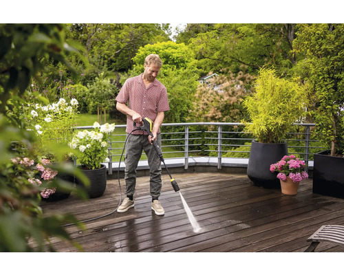Man reinigt houten terras met hogedrukreiniger in de tuin.