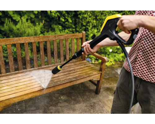 Een persoon reinigt een houten bank met een hogedrukreiniger.