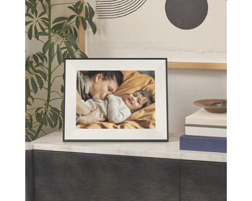 Een zwarte fotolijst met witte passe-partout op een marmeren dressoir, met boeken en een groene kamerplant.
