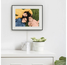 Digitale fotolijst met zwarte lijst gemonteerd op een witte muur boven een witte commode.