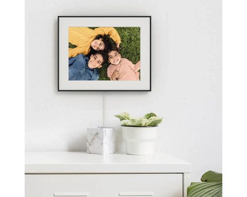 Digitale fotolijst met zwarte lijst gemonteerd op een witte muur boven een witte commode.