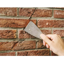 Een hand vult een scheur in een bakstenen muur met vulmiddel