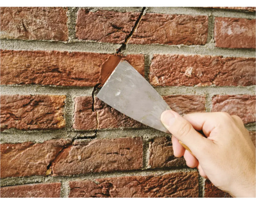 Een hand vult een scheur in een bakstenen muur met vulmiddel