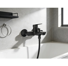 Zwarte badkraan met handdouche en badkameraccessoires aan de muur boven het bad.