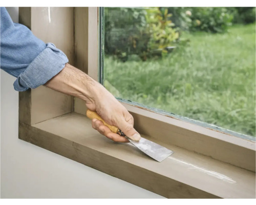 Een persoon gebruikt een plamuurmes om voegmiddel op een vensterbank aan te brengen.