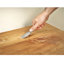 Hand met plamuurmes om een houten oppervlak te repareren