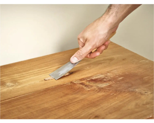 Hand met plamuurmes om een houten oppervlak te repareren