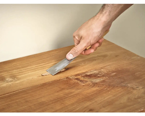 Hand met plamuurmes bij het repareren van een houten tafel.