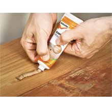 Een vakman vult met houtplamuur uit een tube een gat in het hout.