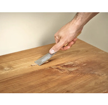 Hand met plamuurmes bij het repareren van houten meubels.