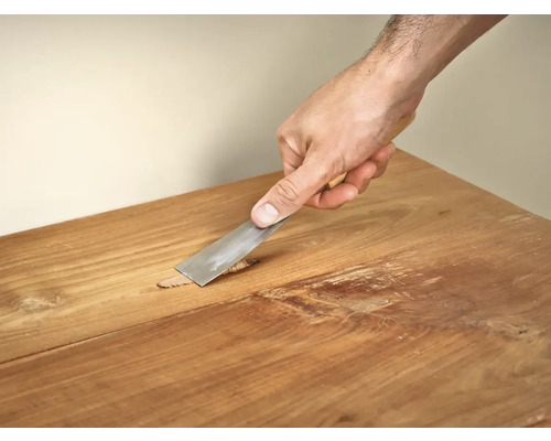 Hand met plamuurmes bij het repareren van houten meubels.