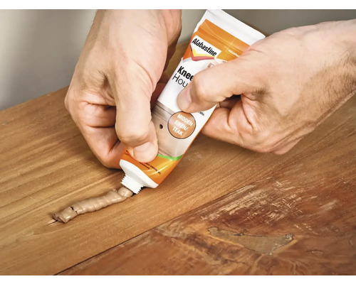 Iemand vult een houtreparatiemiddel uit een tube in een scheur in het hout.