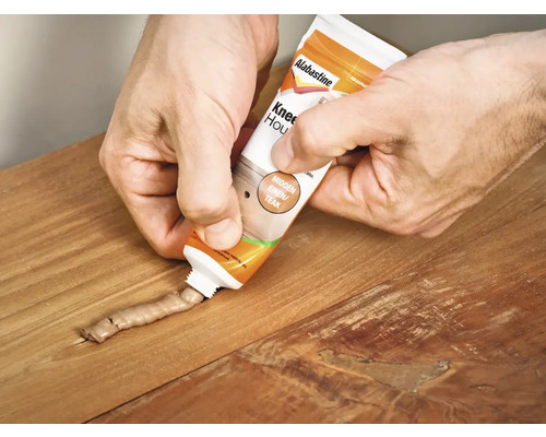 Een persoon vult een houtreparatiemassa uit een tube op een houten oppervlak