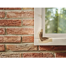 Beschadigd houten raamkozijn naast een bakstenen muur